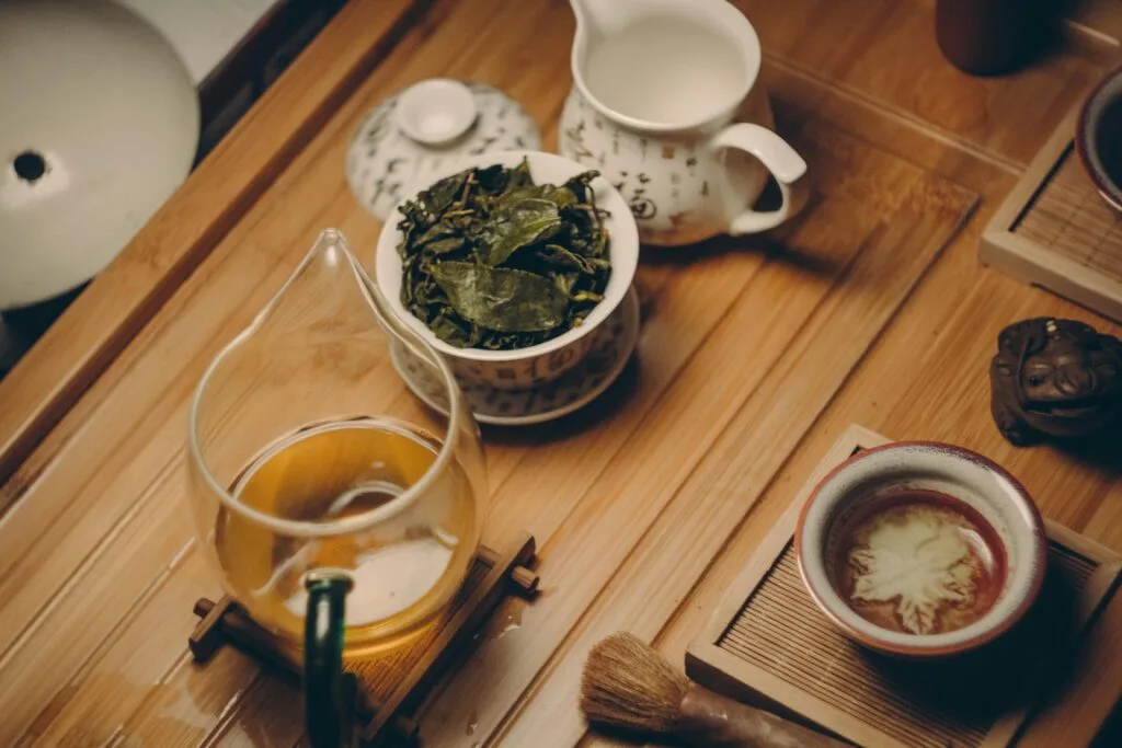 Warm, inviting tea ceremony scene with traditional teapot, leaves, and cup on a wooden table.