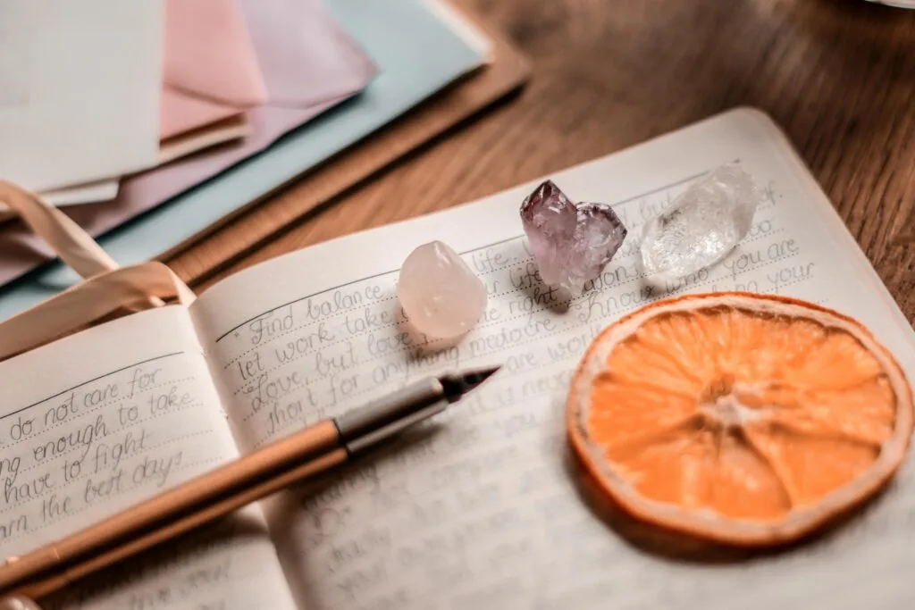 Aesthetic journal scene featuring crystals, a pen, and a dried orange slice on a wooden table.