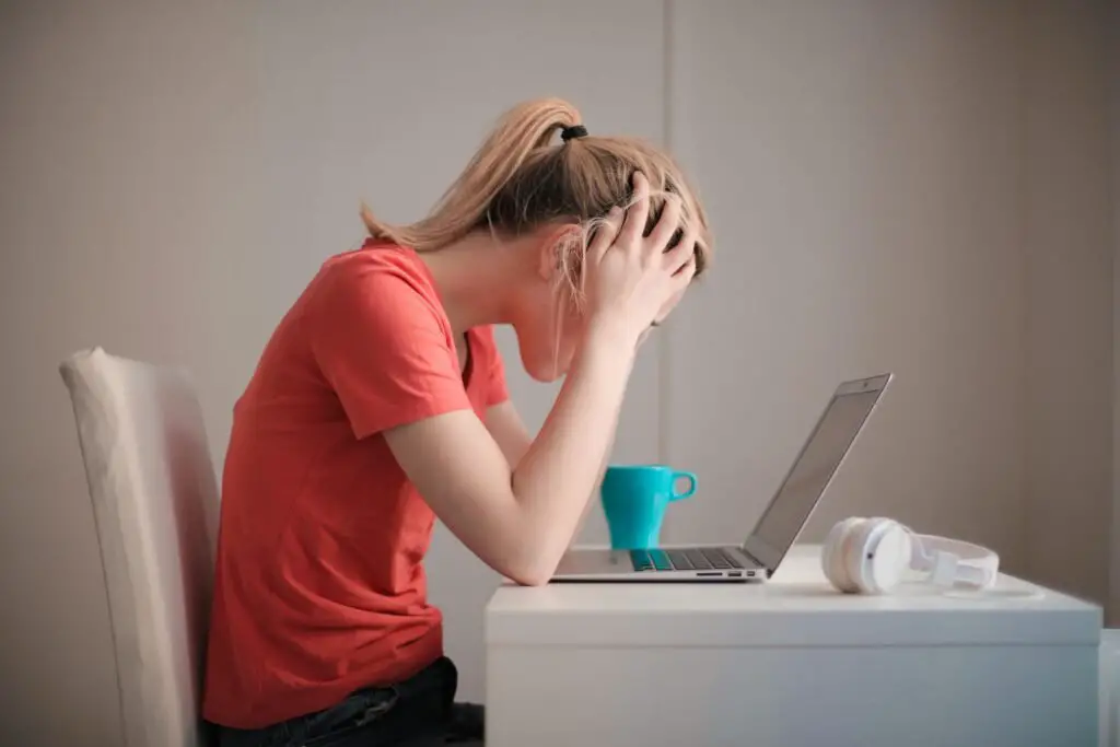 Young woman feeling stressed while studying at home with a laptop and coffee cup.