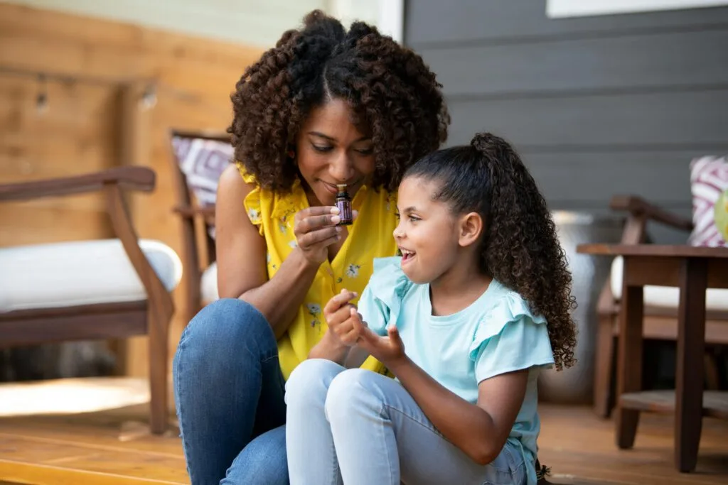 A mother and daughter share a joyful moment using essential oils on a porch.