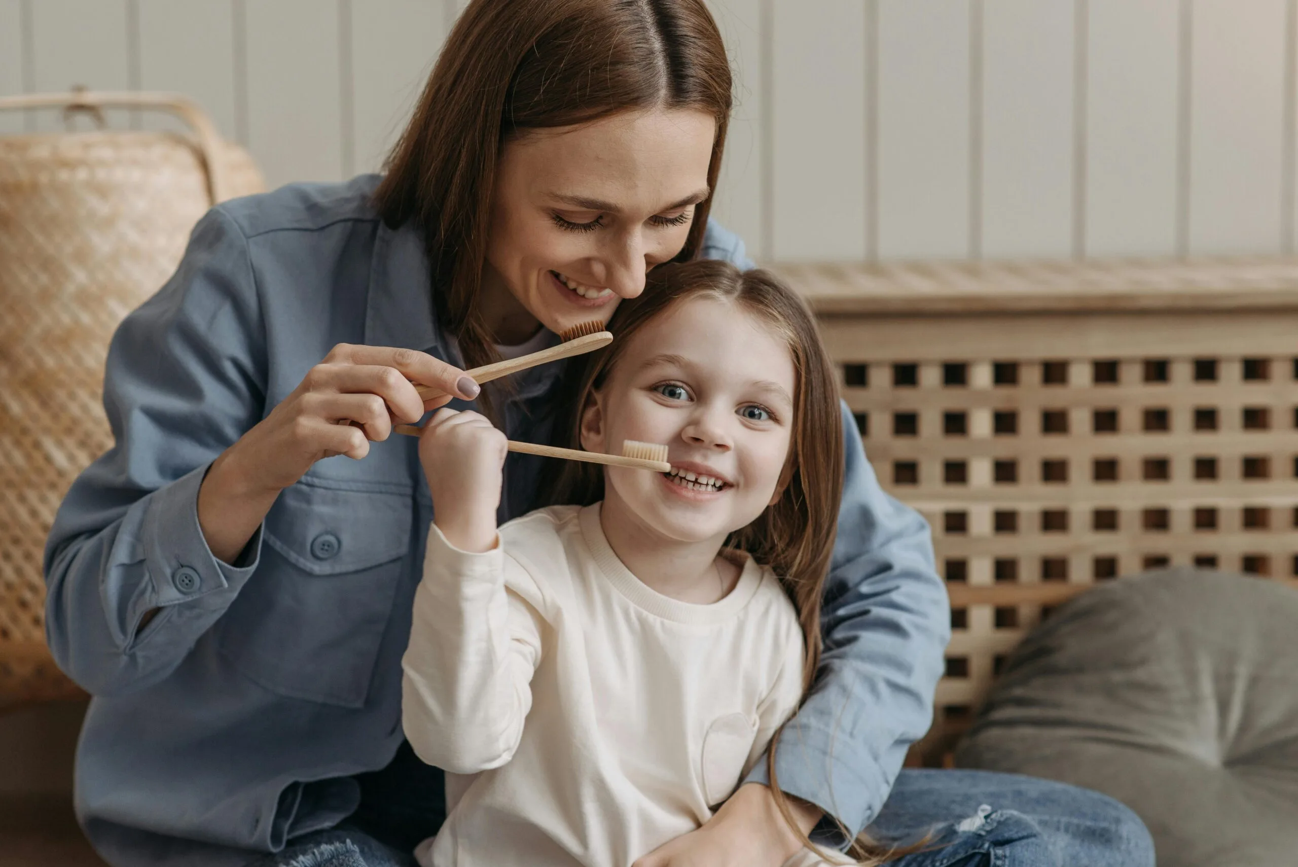 A joyful moment of a mother helping her daughter brush teeth indoors.