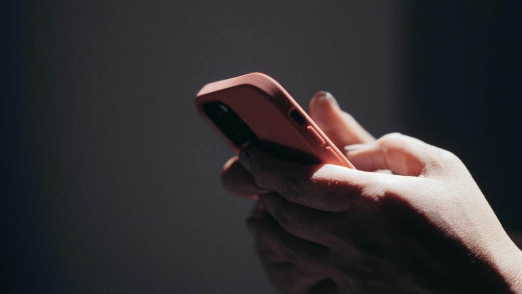 Close-up of hands holding a smartphone in dim lighting, showcasing texting or browsing activity.